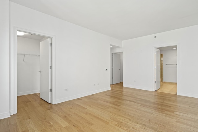 unfurnished bedroom featuring a walk in closet, light wood-style floors, and baseboards