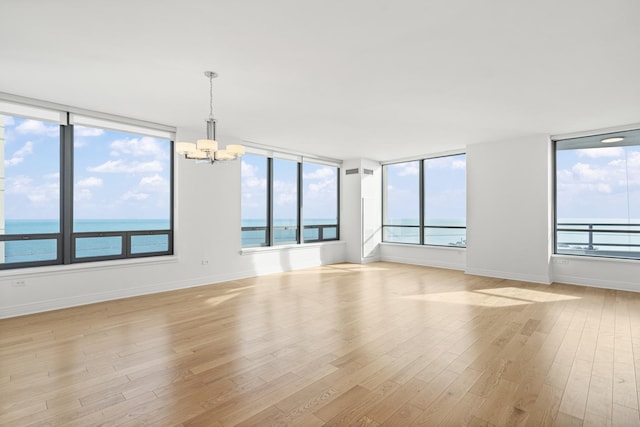 spare room featuring light wood-type flooring, baseboards, an inviting chandelier, and a healthy amount of sunlight