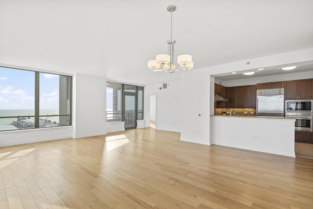 unfurnished living room with an inviting chandelier, visible vents, light wood-type flooring, and baseboards