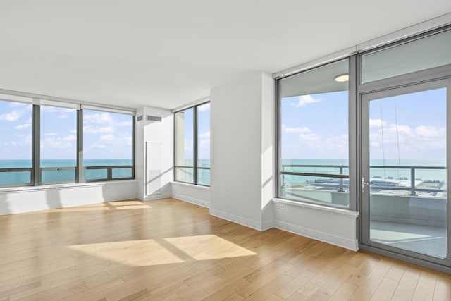 spare room featuring light wood-style floors, a water view, and baseboards