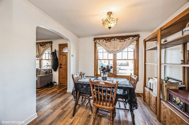 dining room with baseboards, wood finished floors, arched walkways, and ornamental molding