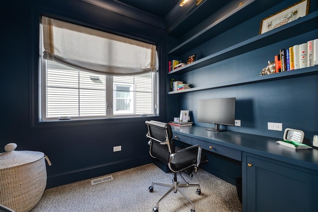 carpeted office space with visible vents, built in shelves, baseboards, and built in study area