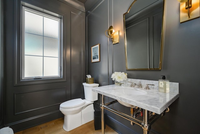 half bathroom featuring toilet, wood finished floors, and a sink