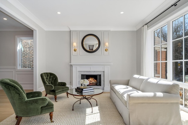 living area with wood finished floors, a premium fireplace, recessed lighting, crown molding, and a decorative wall