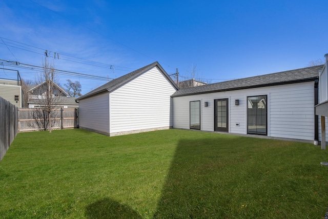 back of house featuring a lawn, roof with shingles, and a fenced backyard