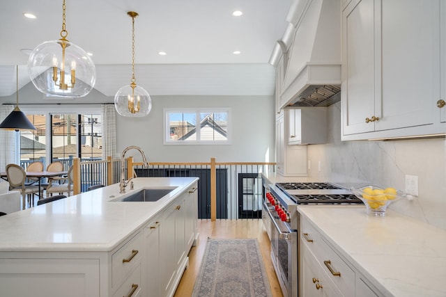 kitchen featuring high end stove, custom range hood, a sink, tasteful backsplash, and light wood-style floors