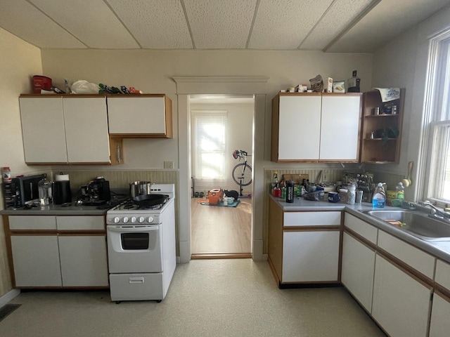 kitchen with white cabinetry, white range with gas stovetop, light floors, and a sink