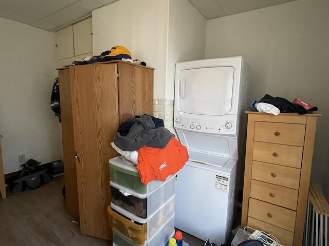 clothes washing area featuring laundry area, stacked washer and dryer, and wood finished floors