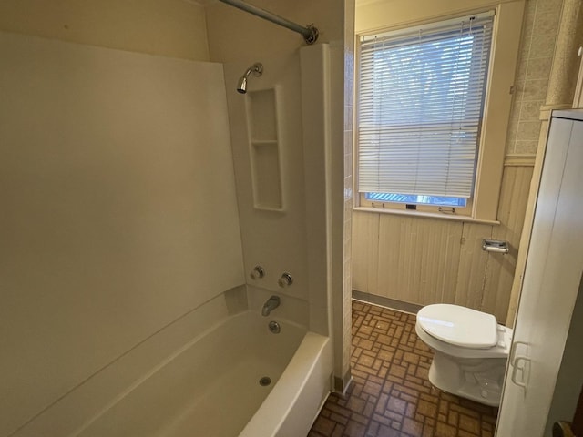 bathroom featuring  shower combination, wooden walls, toilet, and a healthy amount of sunlight