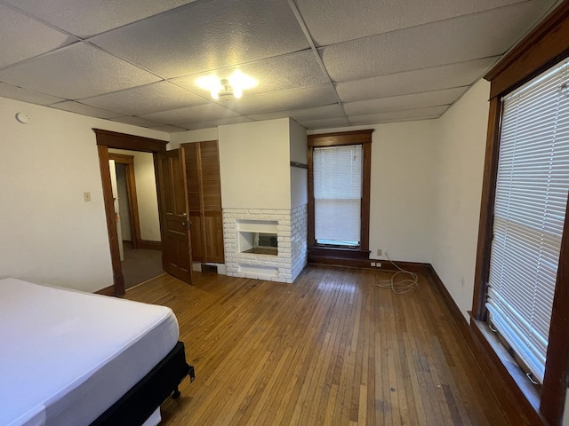 unfurnished bedroom featuring a drop ceiling, a fireplace, baseboards, and wood-type flooring