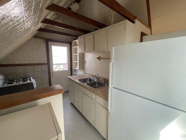 kitchen with lofted ceiling, white cabinets, freestanding refrigerator, and a sink