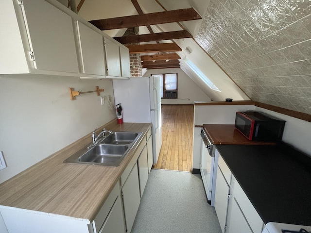 kitchen with a sink, white cabinetry, freestanding refrigerator, and vaulted ceiling