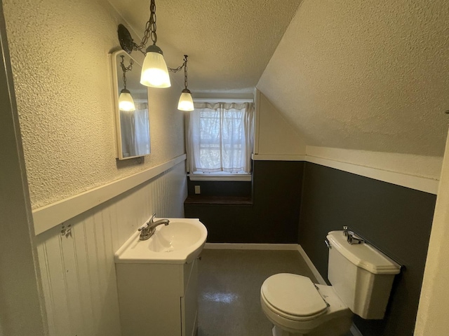 half bath featuring vanity, lofted ceiling, wainscoting, a textured ceiling, and toilet