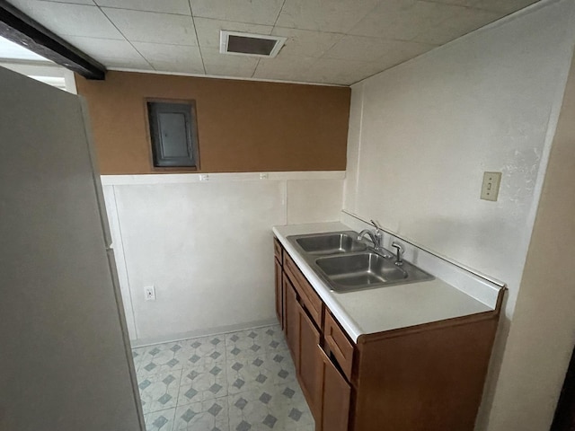 kitchen featuring a sink, electric panel, brown cabinetry, light countertops, and light floors