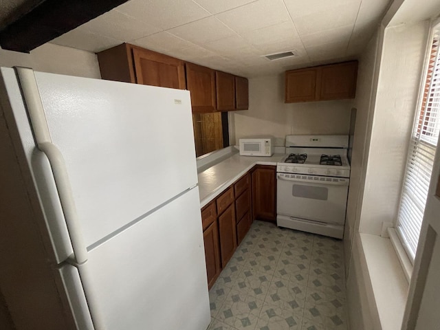 kitchen featuring visible vents, light floors, light countertops, brown cabinets, and white appliances