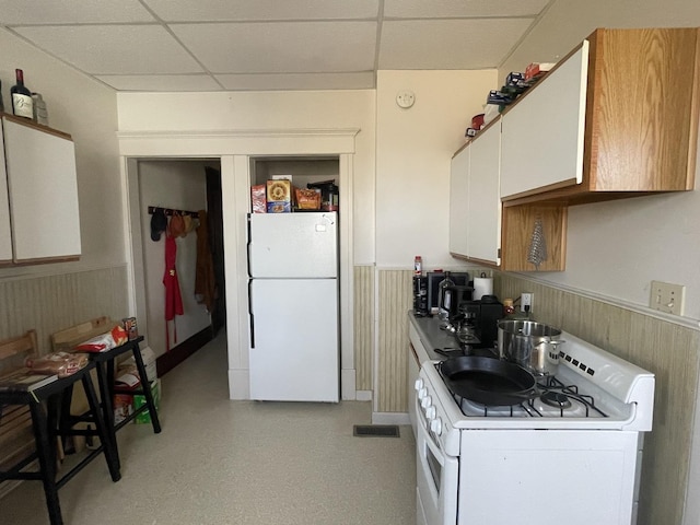 kitchen featuring white appliances, white cabinets, a paneled ceiling, and a wainscoted wall