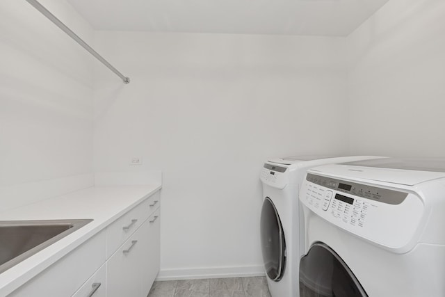 washroom featuring baseboards, cabinet space, a sink, and washer and clothes dryer