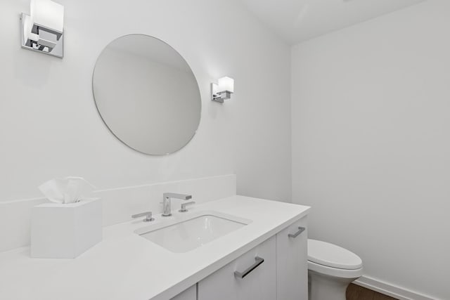 bathroom with toilet, vanity, baseboards, and wood finished floors