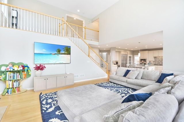 living room featuring baseboards, light wood-type flooring, stairs, recessed lighting, and a high ceiling