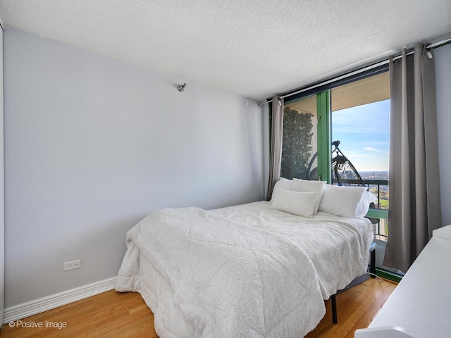 bedroom featuring floor to ceiling windows, a textured ceiling, baseboards, and wood finished floors