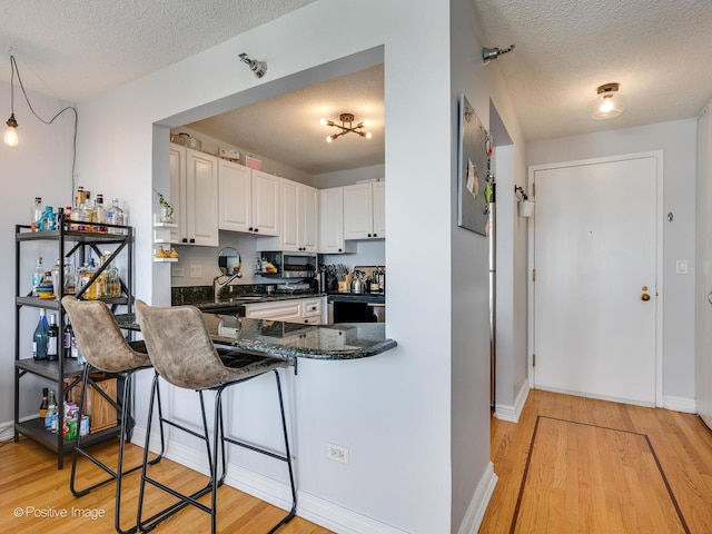 kitchen featuring dark stone countertops, electric range, a textured ceiling, white cabinetry, and light wood-type flooring