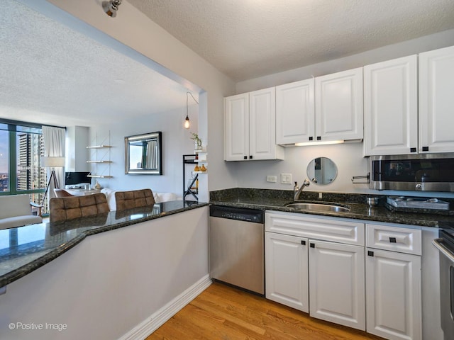 kitchen featuring dark stone countertops, light wood finished floors, a sink, white cabinets, and appliances with stainless steel finishes