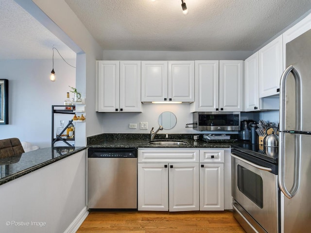 kitchen featuring dark stone counters, light wood-style flooring, stainless steel appliances, white cabinetry, and a sink