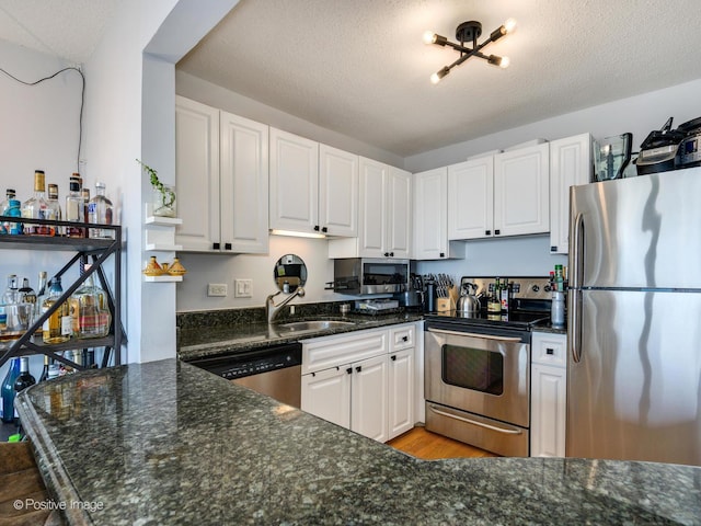 kitchen featuring white cabinetry, dark stone countertops, appliances with stainless steel finishes, and a sink