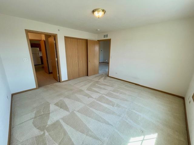 bedroom featuring visible vents, baseboards, light colored carpet, freestanding refrigerator, and a closet