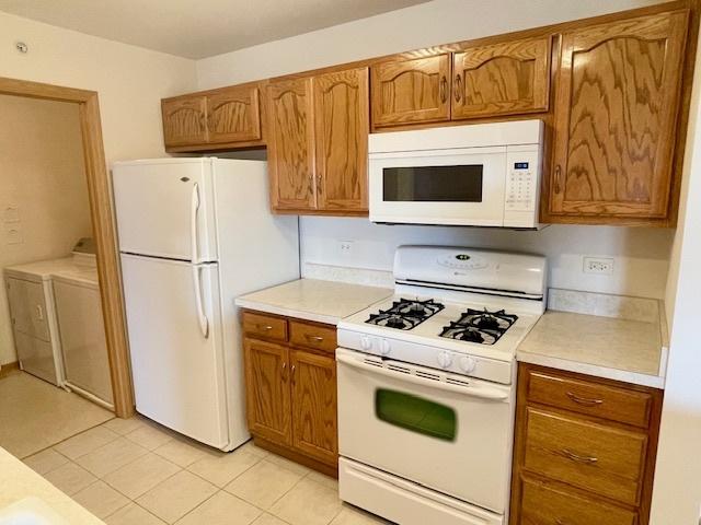 kitchen featuring independent washer and dryer, white appliances, light countertops, and brown cabinets