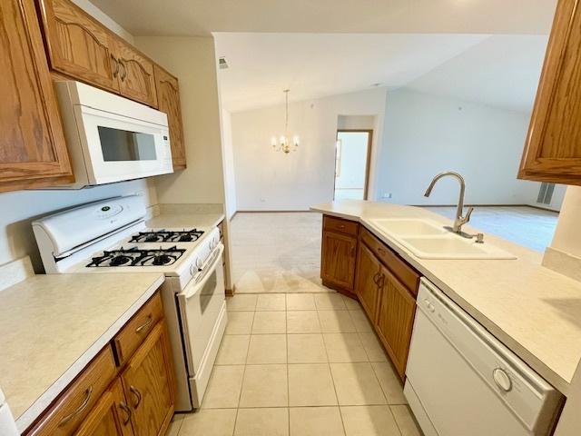 kitchen with white appliances, brown cabinetry, a sink, vaulted ceiling, and light countertops