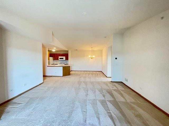 unfurnished living room with a sink, baseboards, light carpet, and a notable chandelier