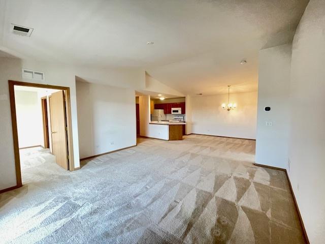 unfurnished living room with lofted ceiling, a notable chandelier, visible vents, and light carpet