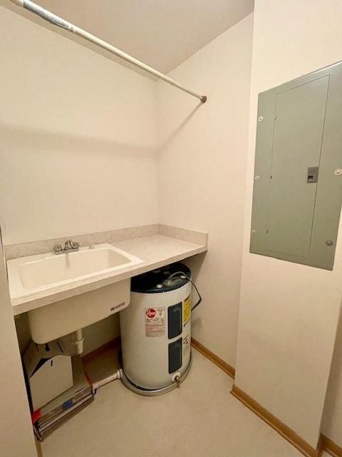 utility room with electric panel, water heater, and a sink