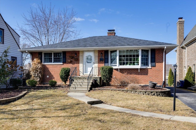 view of front facade with brick siding, a chimney, a front yard, and roof with shingles