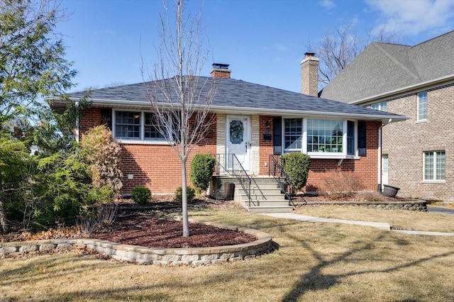 view of front of home with a shingled roof, a front yard, brick siding, and a chimney