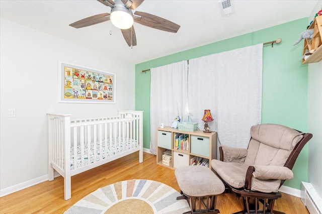 bedroom featuring a nursery area, wood finished floors, visible vents, and baseboards