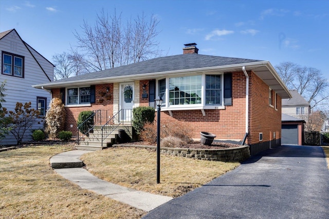 view of front of house featuring an outbuilding, a front yard, a garage, brick siding, and a chimney