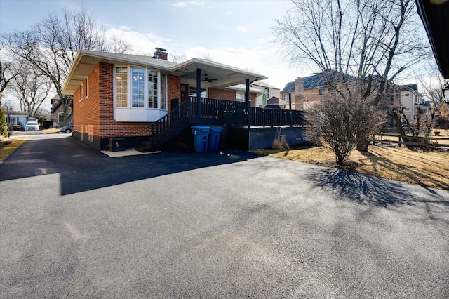 view of front of home with a ceiling fan, driveway, brick siding, and a chimney