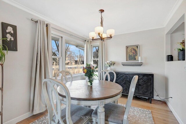 dining room featuring light wood-type flooring, baseboards, a notable chandelier, and ornamental molding