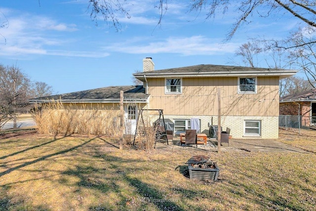 rear view of property featuring fence, an outdoor fire pit, a yard, a chimney, and brick siding