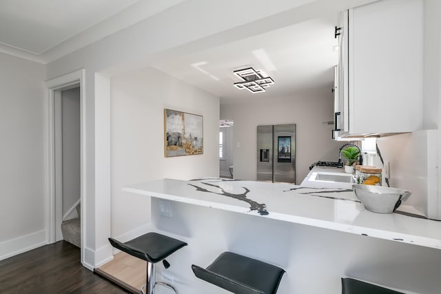 kitchen with dark wood-type flooring, a breakfast bar, stainless steel refrigerator with ice dispenser, white cabinetry, and light countertops