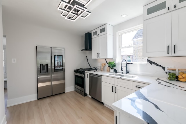 kitchen with a sink, stainless steel appliances, wall chimney exhaust hood, white cabinets, and glass insert cabinets