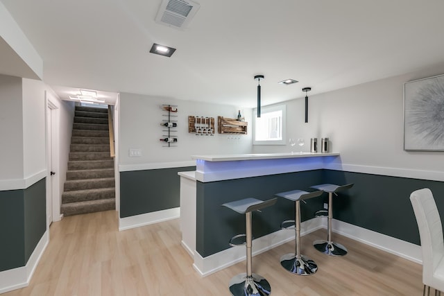 bar featuring visible vents, pendant lighting, stairs, and light wood-style floors