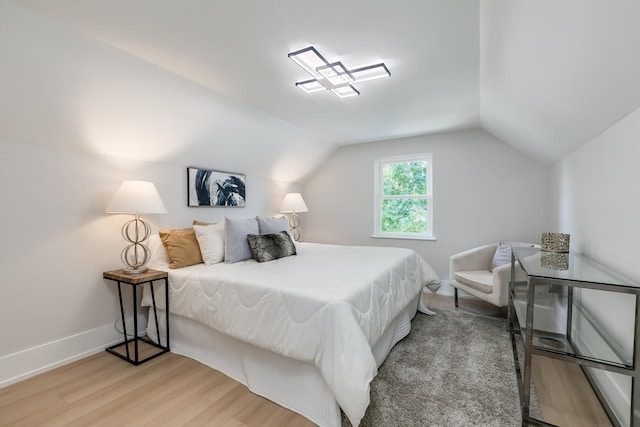 bedroom with light wood finished floors, baseboards, and lofted ceiling