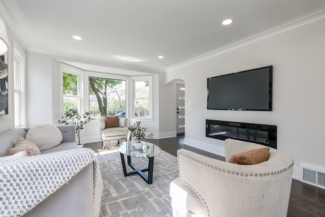 living area with visible vents, arched walkways, wood finished floors, and crown molding