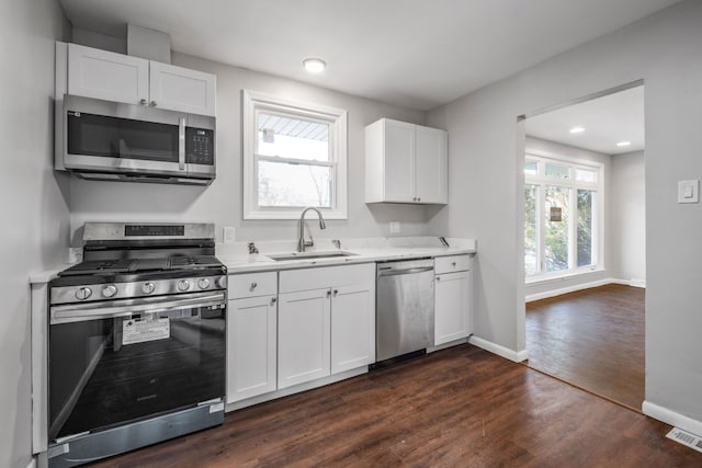 kitchen with dark wood-type flooring, baseboards, light countertops, stainless steel appliances, and a sink