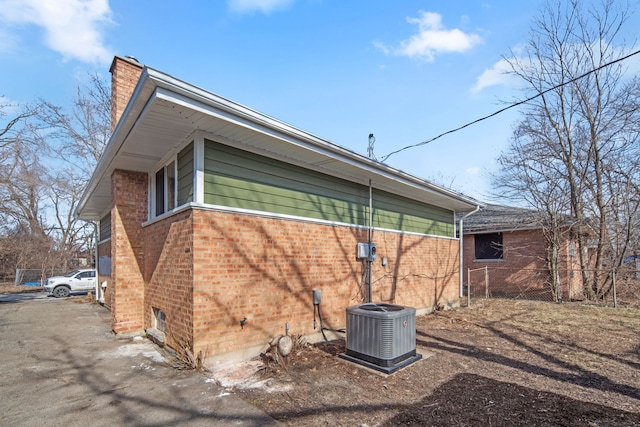 view of home's exterior featuring a chimney, brick siding, fence, and central AC unit