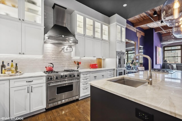 kitchen with beamed ceiling, a sink, backsplash, stainless steel appliances, and wall chimney range hood