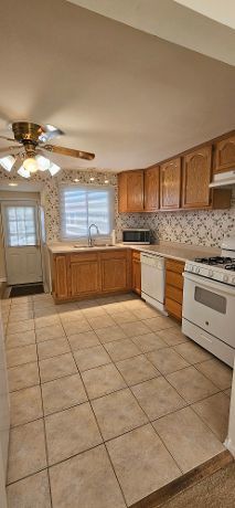 kitchen featuring a sink, under cabinet range hood, white appliances, decorative backsplash, and ceiling fan